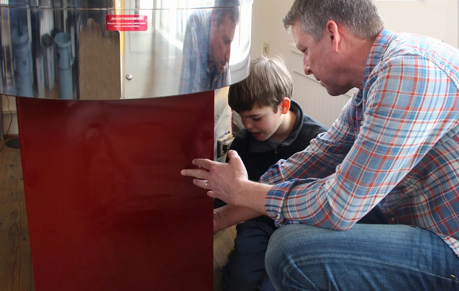 A father and son crouched together at the red drum roaster, watching a batch roast